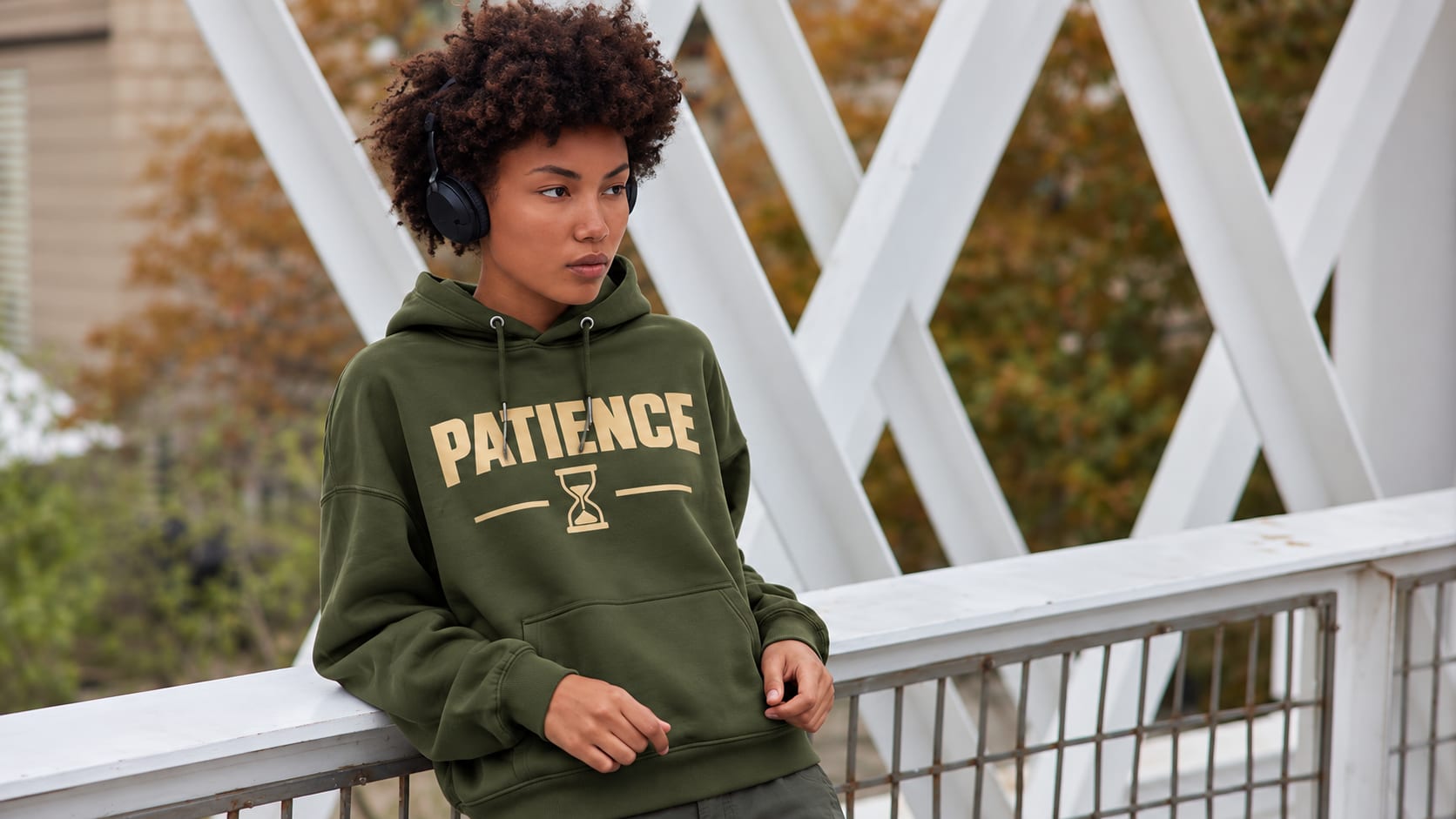Woman in an olive Patience hoodie on a bridge