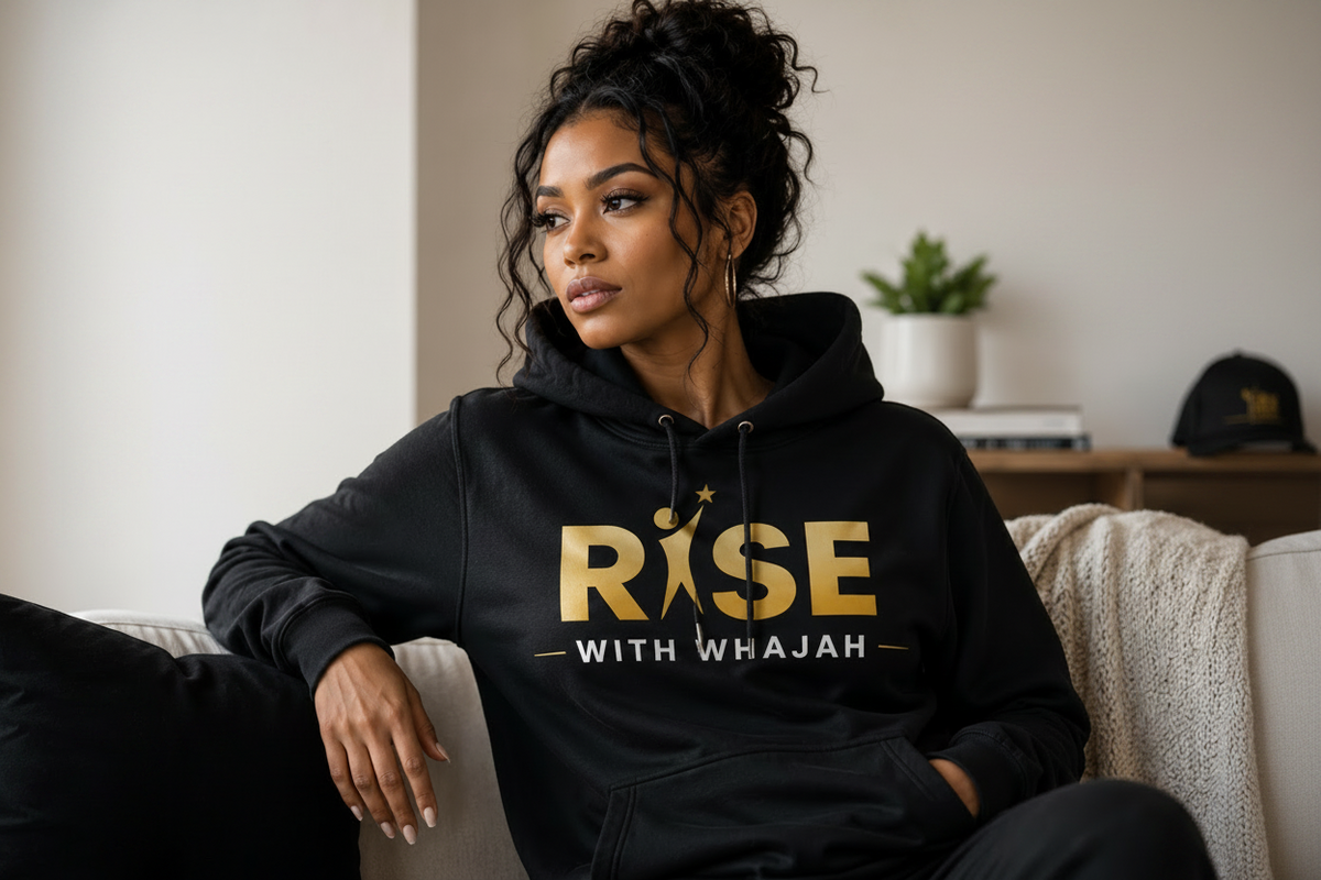 Woman wearing a black Rise With Whajah hoodie with gold lettering, sitting at home