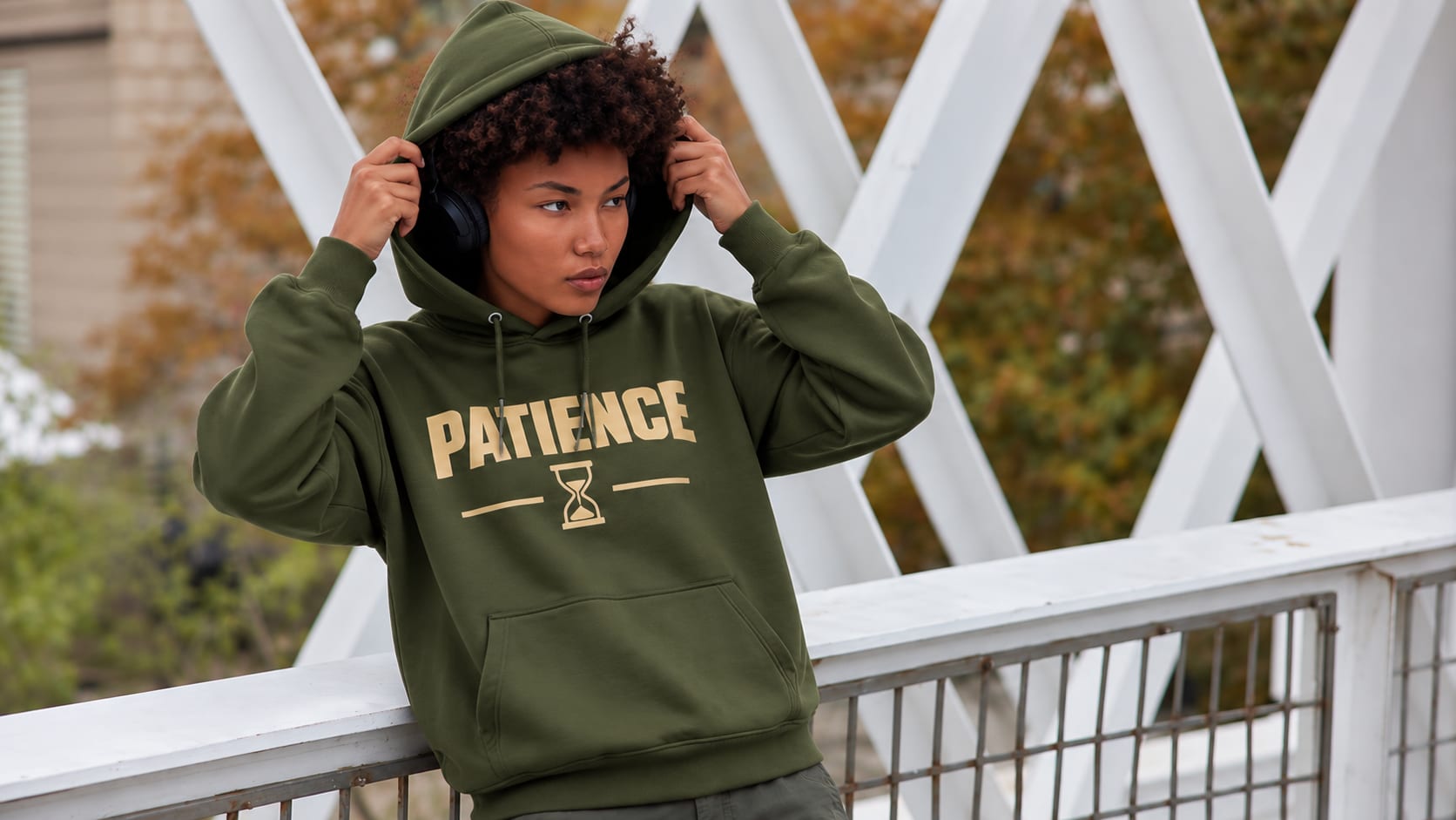 Woman in an olive Patience hoodie pulling on her hood